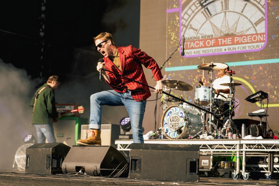 Ricky Wilson of Kaiser Chiefs performs on stage, holding a microphone.