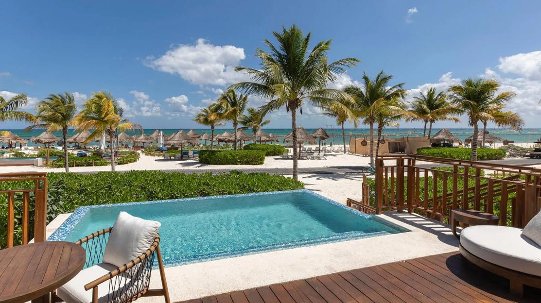 A private pool at Fairmont Mayakoba overlooking the beach with palm trees and thatched umbrellas.