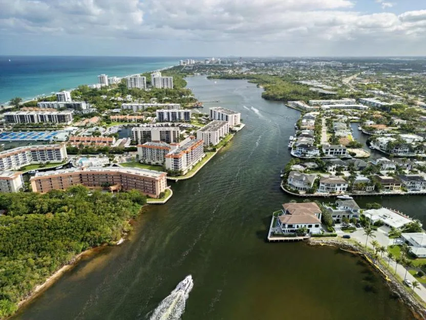 Aerial view of luxury waterfront apartments and residential homes along the Intracoastal Waterway in Boca Raton, Florida, with a boat cruising through the channel.