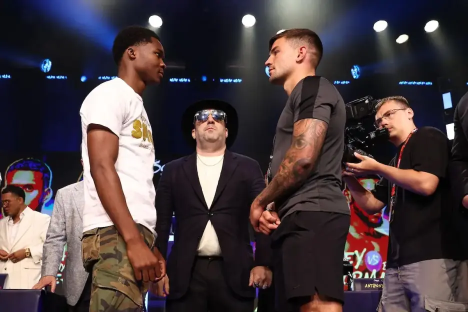 Two male boxers facing each other with a man in a hat and sunglasses in the middle.