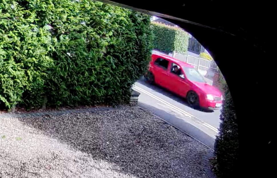 A red Volkswagen Golf speeds past a green hedge, captured from a Ring doorbell camera.