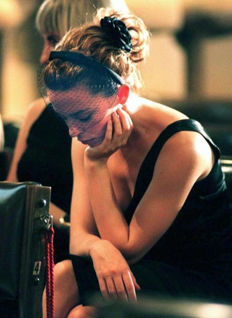 Kylie Minogue sitting with her head bowed and hands clasped at a funeral.