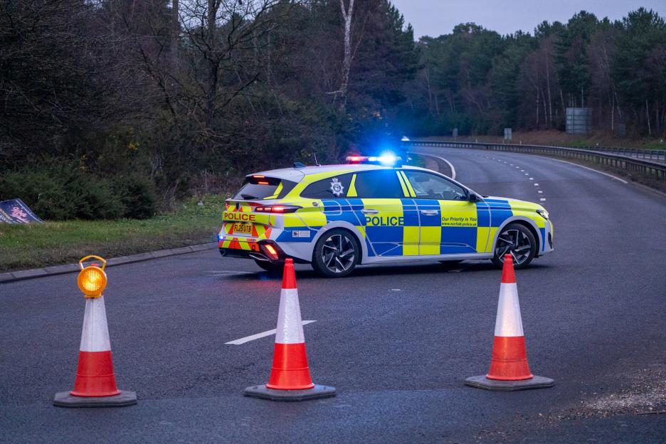 Police car with flashing lights and traffic cones blocking a road in Thetford, Norfolk.