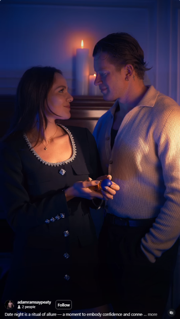 A woman in a black jacket holding a blue and gold object, looking at a man in a beige sweater, both illuminated by candlelight.