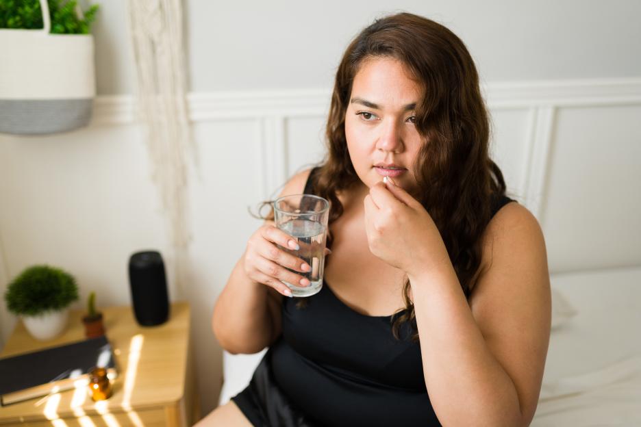 A woman taking a pill with a glass of water.