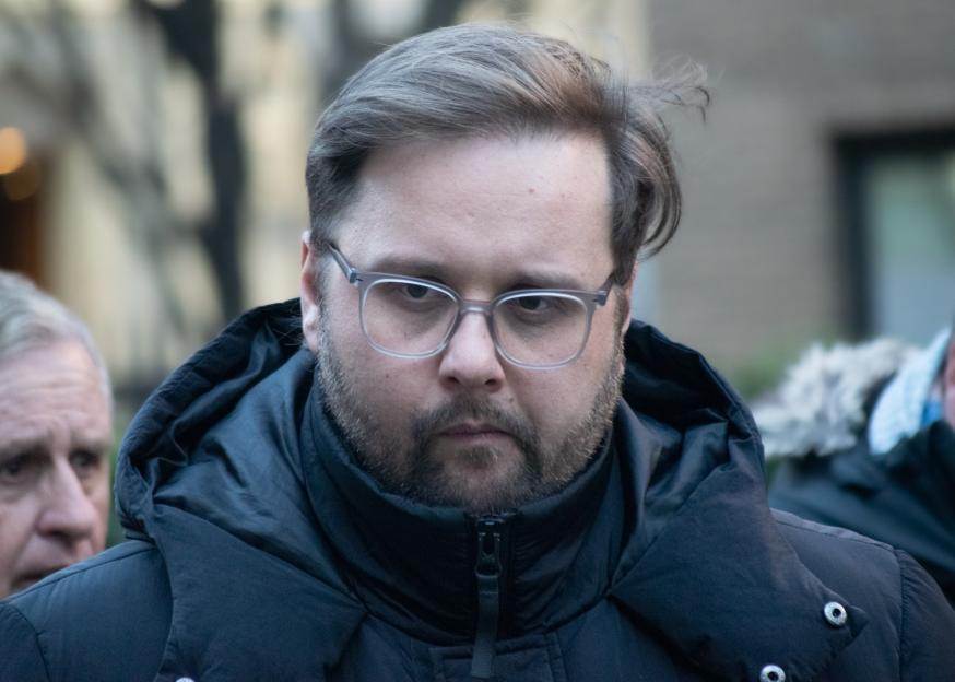 Liam Newman, a police officer with a beard and glasses, wearing a dark puffer coat.