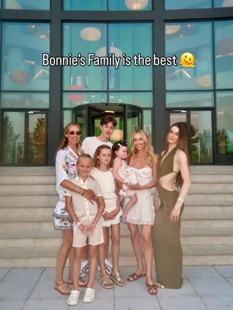 A family of six adults and two children stand together on steps outside a building.