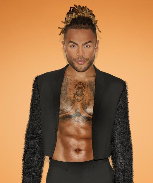 Nathan Henry posing in a black cropped blazer with textured sleeves, showing his tattooed chest and abdomen, against an orange background.