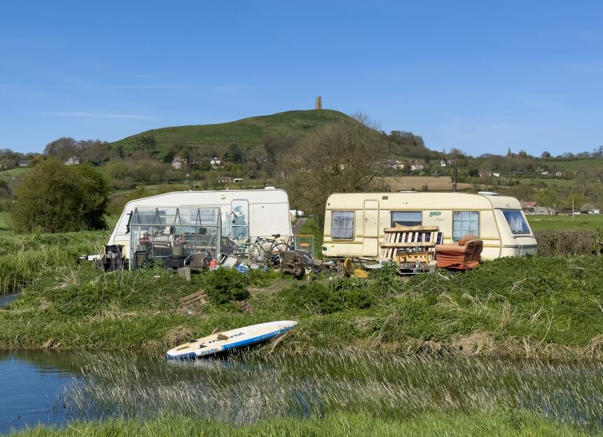 Two caravans parked on grassy banks next to a narrow canal, with Glastonbury Tor in the background.