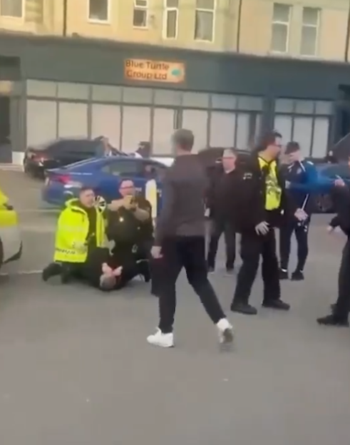 Police officers arresting a man on the ground as other officers and civilians stand nearby.