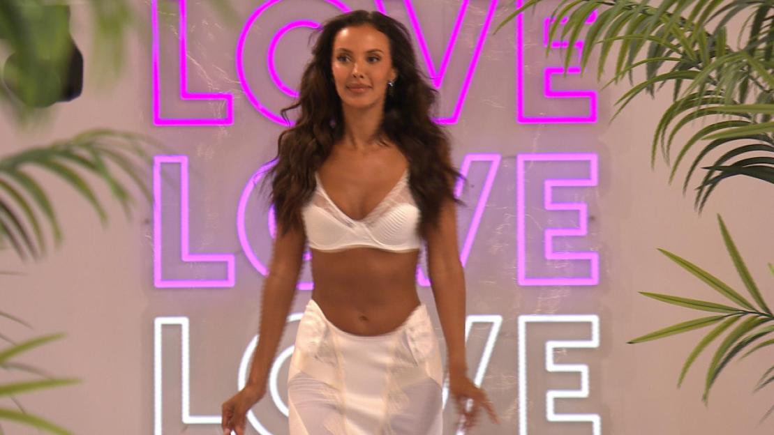 Maya Jama walking in front of a neon sign that says "LOVE."