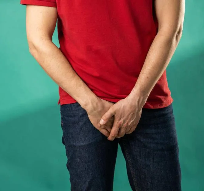 A man holding his hands over his crotch.