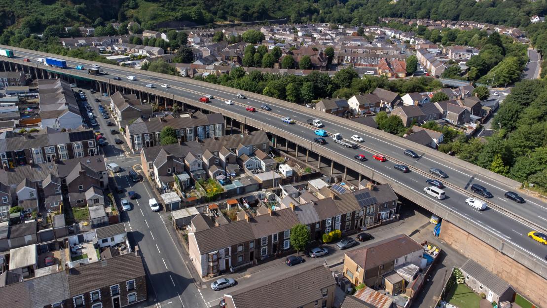 Aerial view of a multi-lane motorway on a raised bridge running above a residential neighborhood.