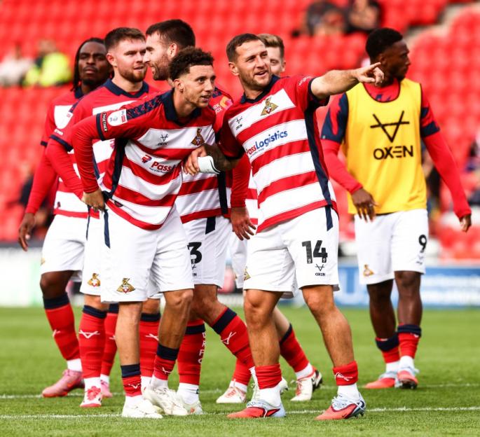 Several male soccer players in red and white striped jerseys and white shorts standing on a field.