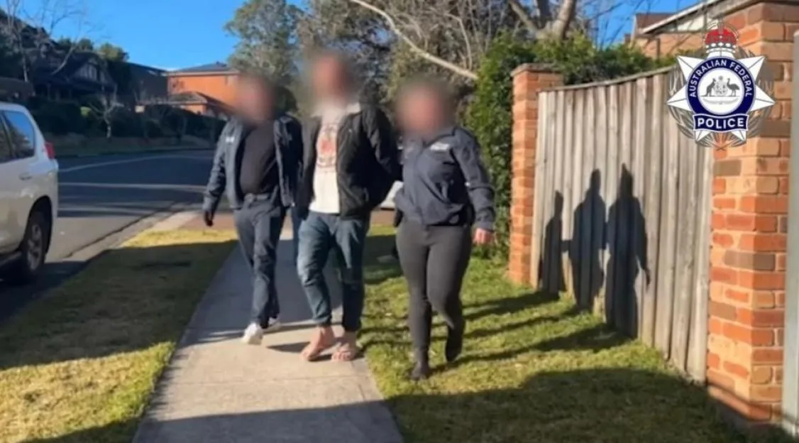 Three individuals, two men and one woman, walk on a sidewalk under the Australian Federal Police logo.