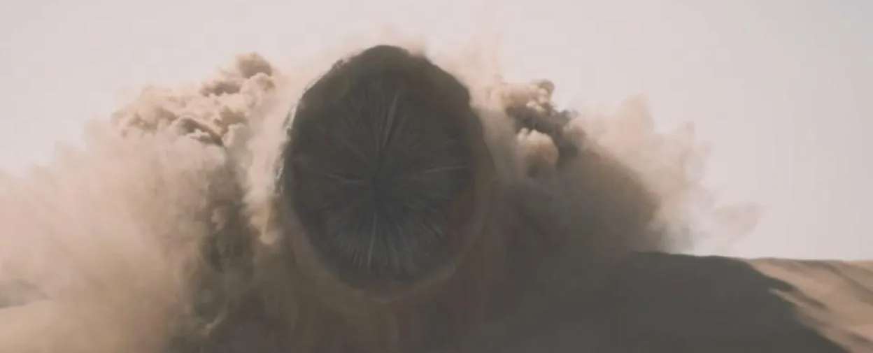 A massive sandworm emerges from a desert dune, surrounded by a cloud of dust.