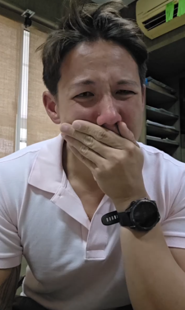 A man in a white polo shirt covering his mouth, crying.