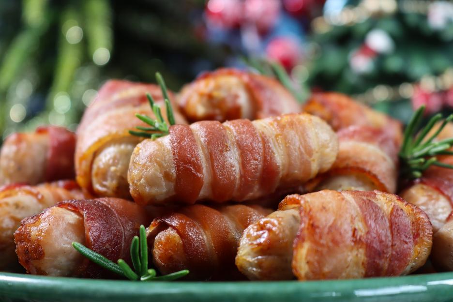 Cooked pigs in blankets on a green plate with rosemary sprigs.