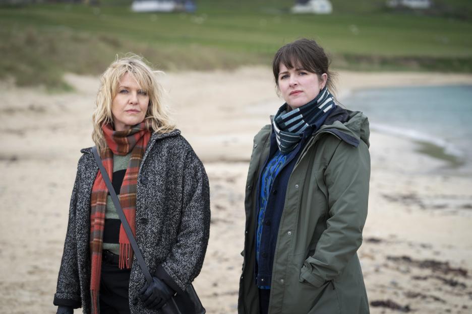 Two women standing on a sandy beach.