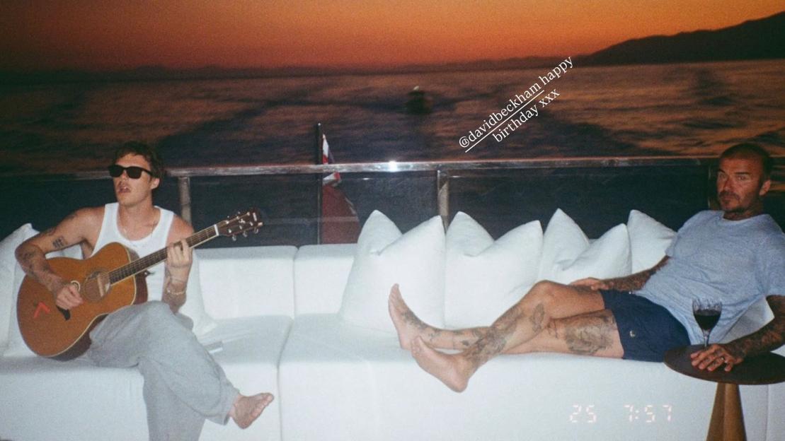 Cruz Beckham playing guitar for David Beckham on a yacht at sunset.