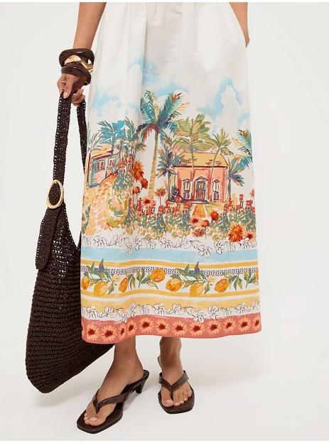 A woman in a white dress with a tropical pattern, brown sandals, and a brown woven bag.