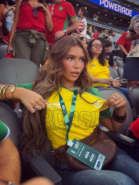 A woman in a "BRASIL" soccer jersey and a pass for a Brazil vs. Morocco match at a stadium.