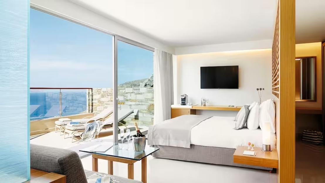 A bright hotel room with a bed and a balcony overlooking the ocean.