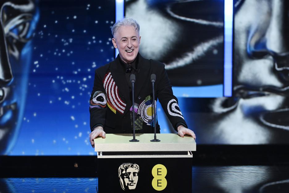 Host Alan Cumming speaking on stage at the EE BAFTA Film Awards 2026.