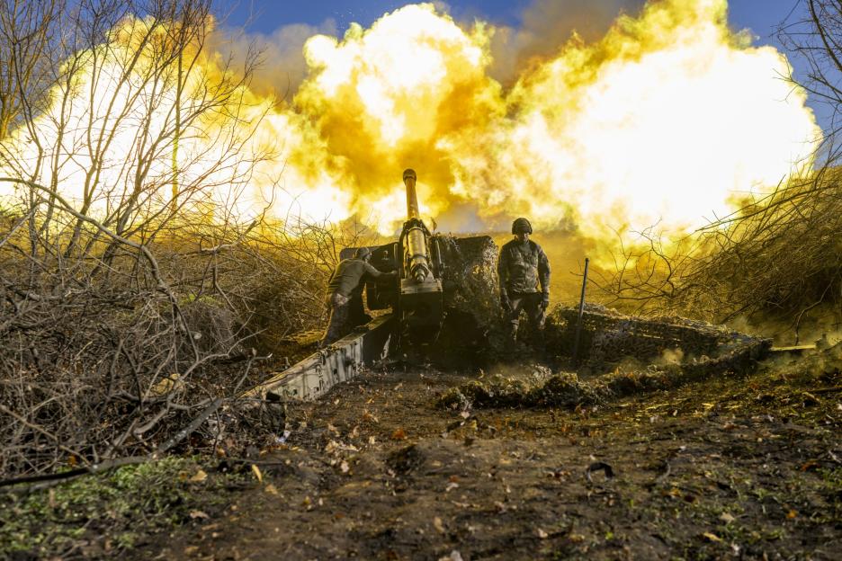 Two soldiers firing an artillery cannon, with a large orange-yellow explosion of smoke and fire billowing from the barrel.