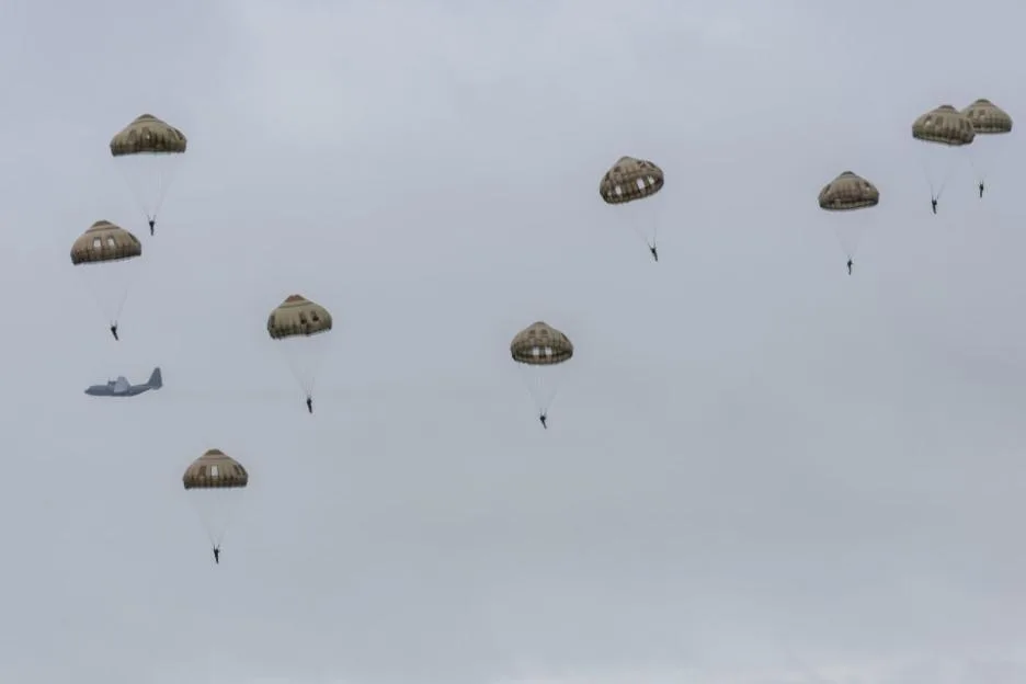 Several paratroopers descend with parachutes while an airplane flies in the background.
