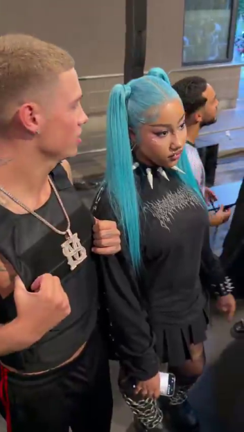 North West in a black shirt, skirt, and chain boots, with a male escort.