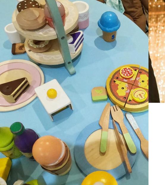 Table covered with various toy foods including a multi-tiered dessert stand, pizza, and hamburger.