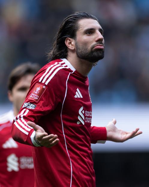 Liverpool player with long dark hair and a beard, wearing a red jersey with the Emirates FA Cup patch, gestures with open hands during the quarter-final match against Manchester City.