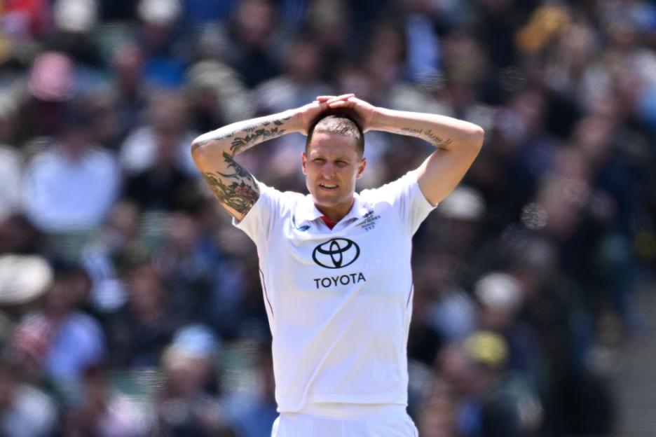 A cricketer in a white uniform with a Toyota logo on his shirt stands with his hands on his head.