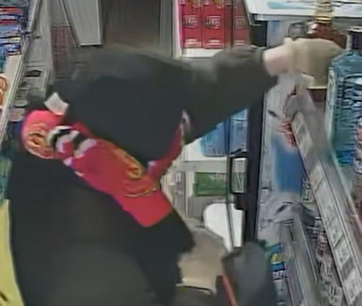 A person wearing a black hoodie and red scarf stealing alcohol from a shop.