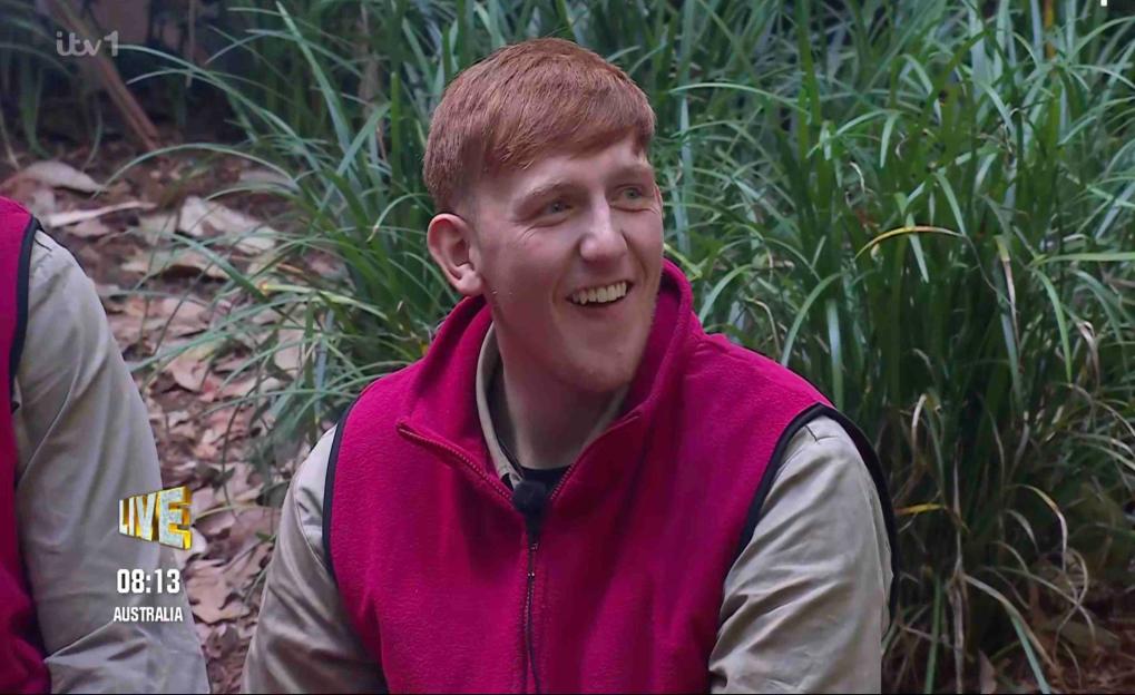 Angry Ginge smiling and wearing a magenta vest over a khaki long-sleeved shirt.