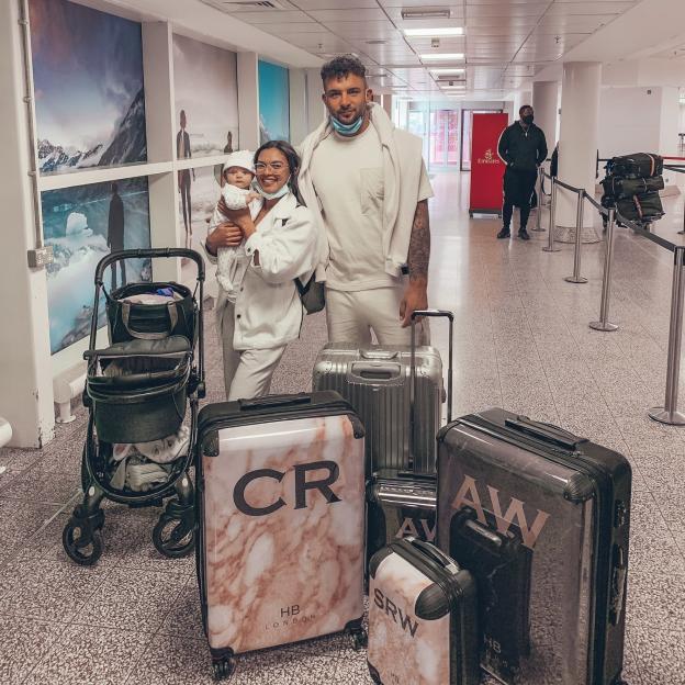 Charlotte Lescott, Ali Watson, and their daughter Soulie with luggage in an airport.