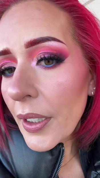 A woman with bright pink hair, pink and blue eyeshadow, and pink lipstick.