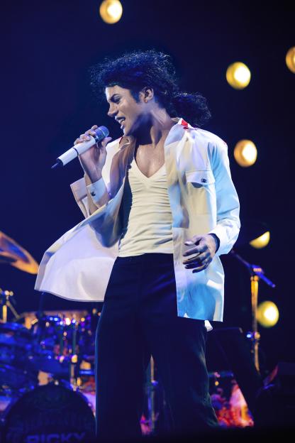 Jaafar Jackson as Michael Jackson, singing on stage in a white shirt and black pants.