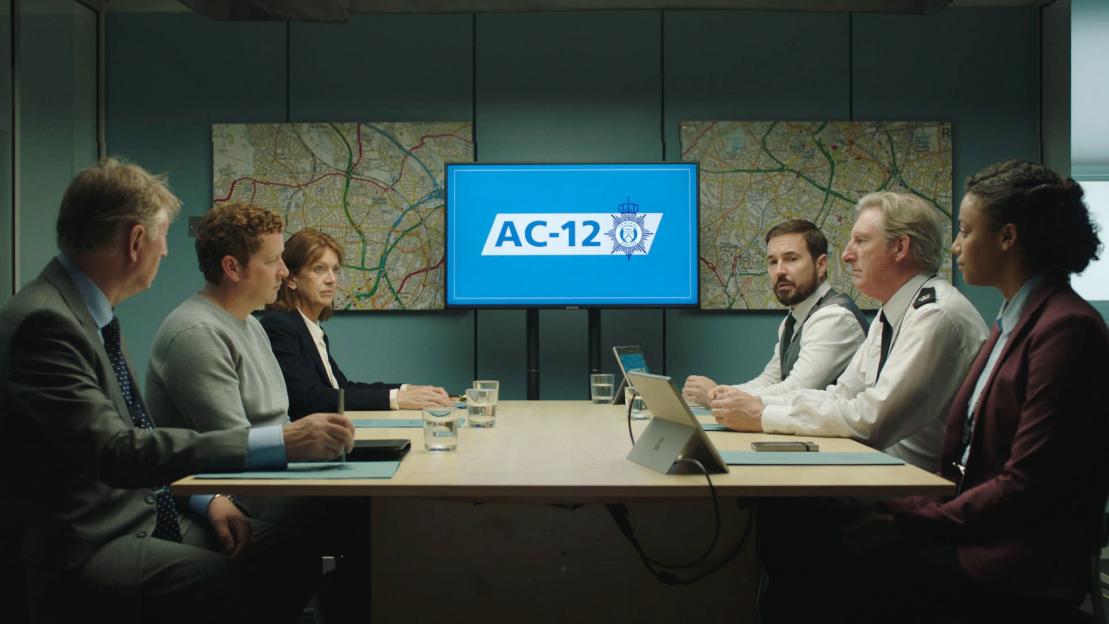 DCI Ian Buckells and his team at a meeting in a room with a monitor displaying "AC-12".