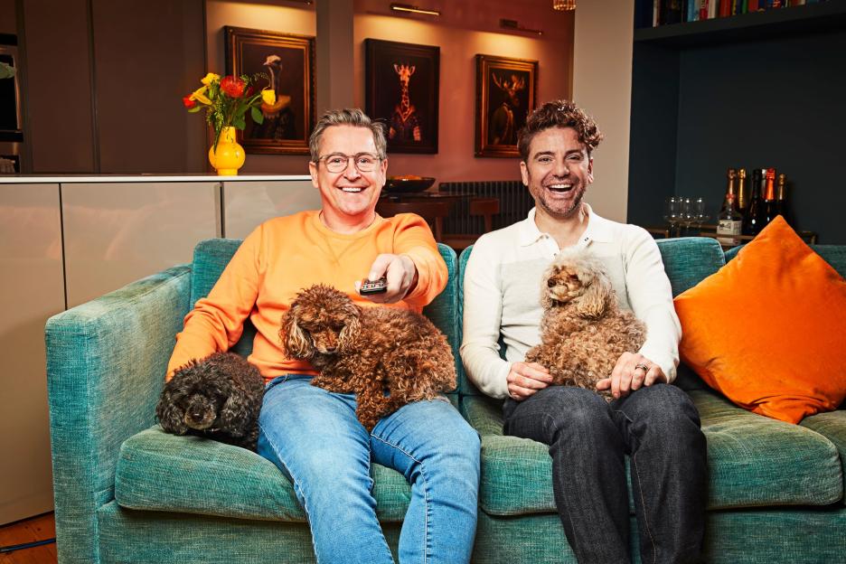 Stephen and Daniel Lustig-Webb with three dogs on a turquoise sofa.