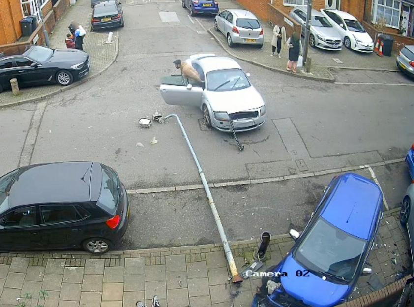 CCTV footage of a silver car crashed into a lamppost, with a blue car severely damaged, and people standing around.