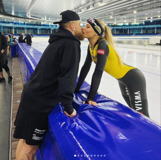 A man and a woman in athletic wear kissing by an ice rink.
