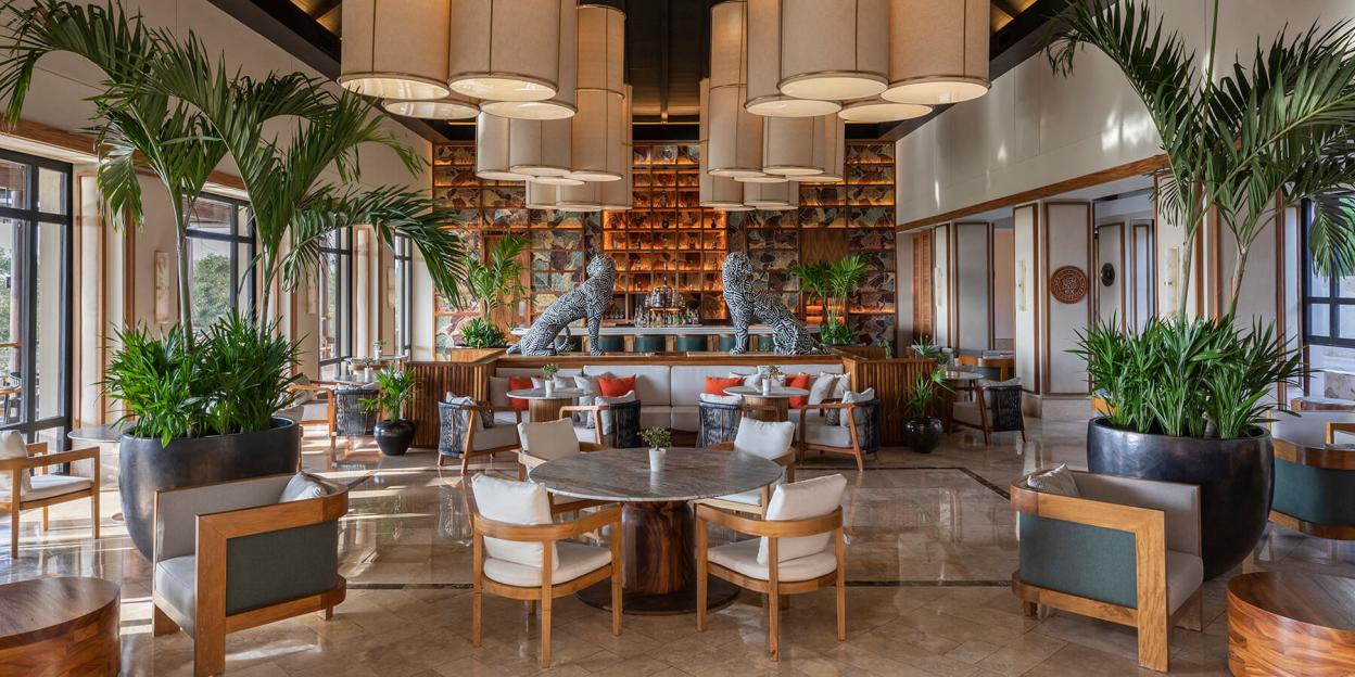 Lobby of the Fairmount Mayakoba luxury hotel with a bar, seating areas, and large potted plants.