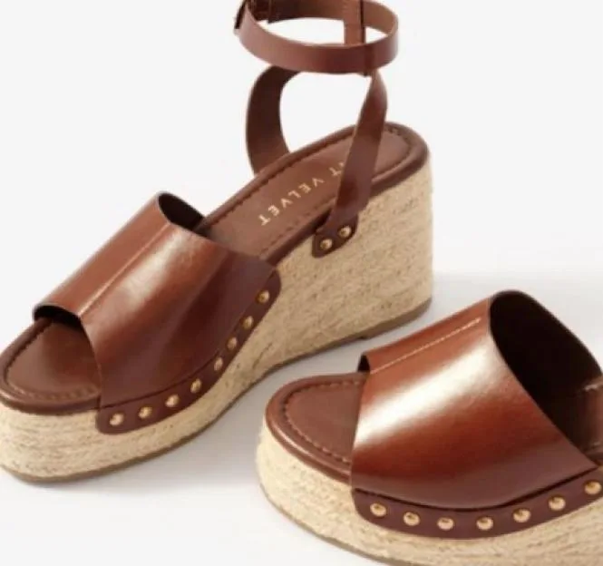 A pair of brown leather wedge sandals with ankle straps and espadrille soles.