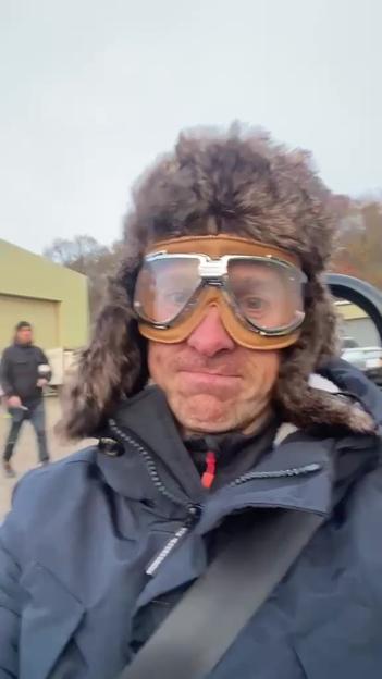 Paul Rees wearing goggles and a fur hat, filming himself in the crashed car from Top Gear.