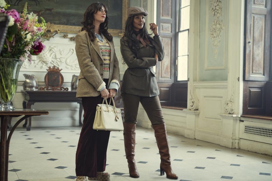 Two women in stylish, country-inspired outfits stand in an opulent room with ornate detailing.