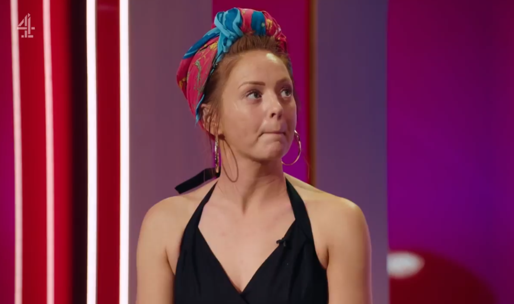 A woman in a black halter top and a colorful headscarf looks upward with a slightly concerned expression.