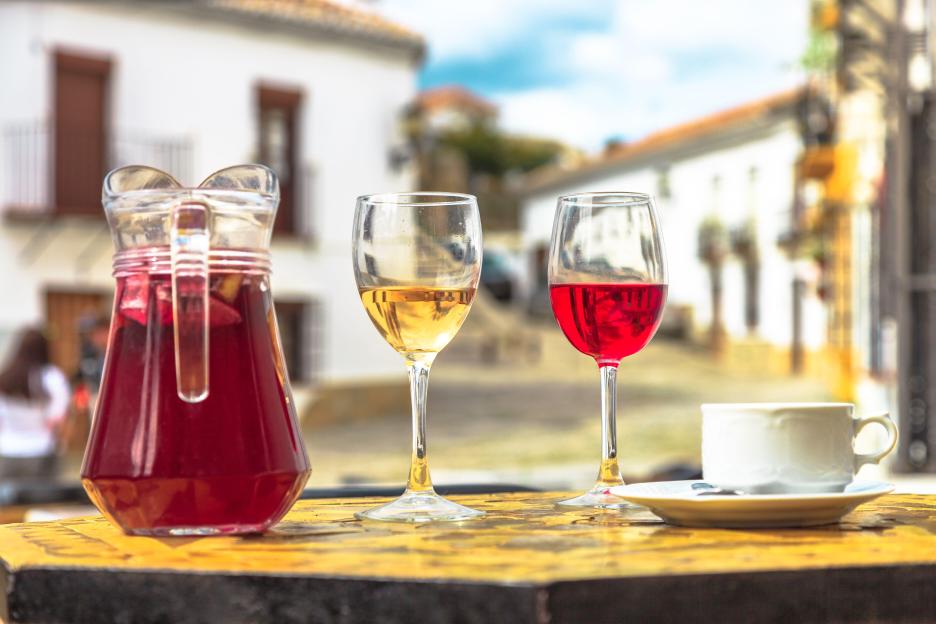 A pitcher of sangria, glasses of red and white wine, and a coffee cup on a table in a Spanish countryside setting.