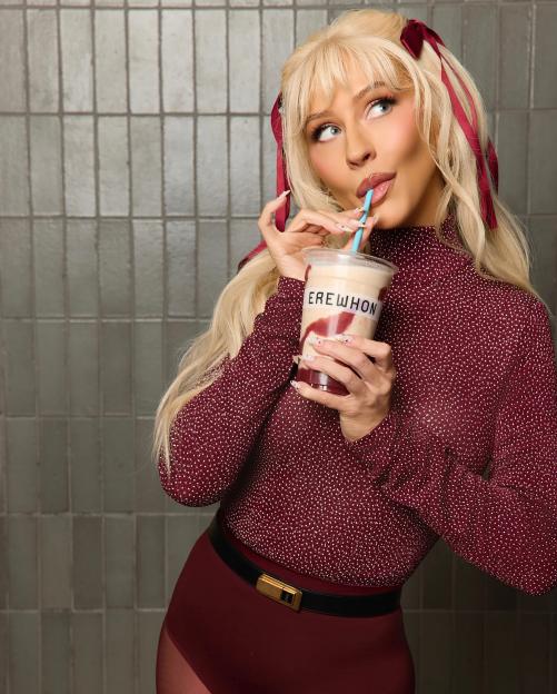Christina Aguilera with an Erewhon smoothie, with blonde hair, red ribbons, and a red top.